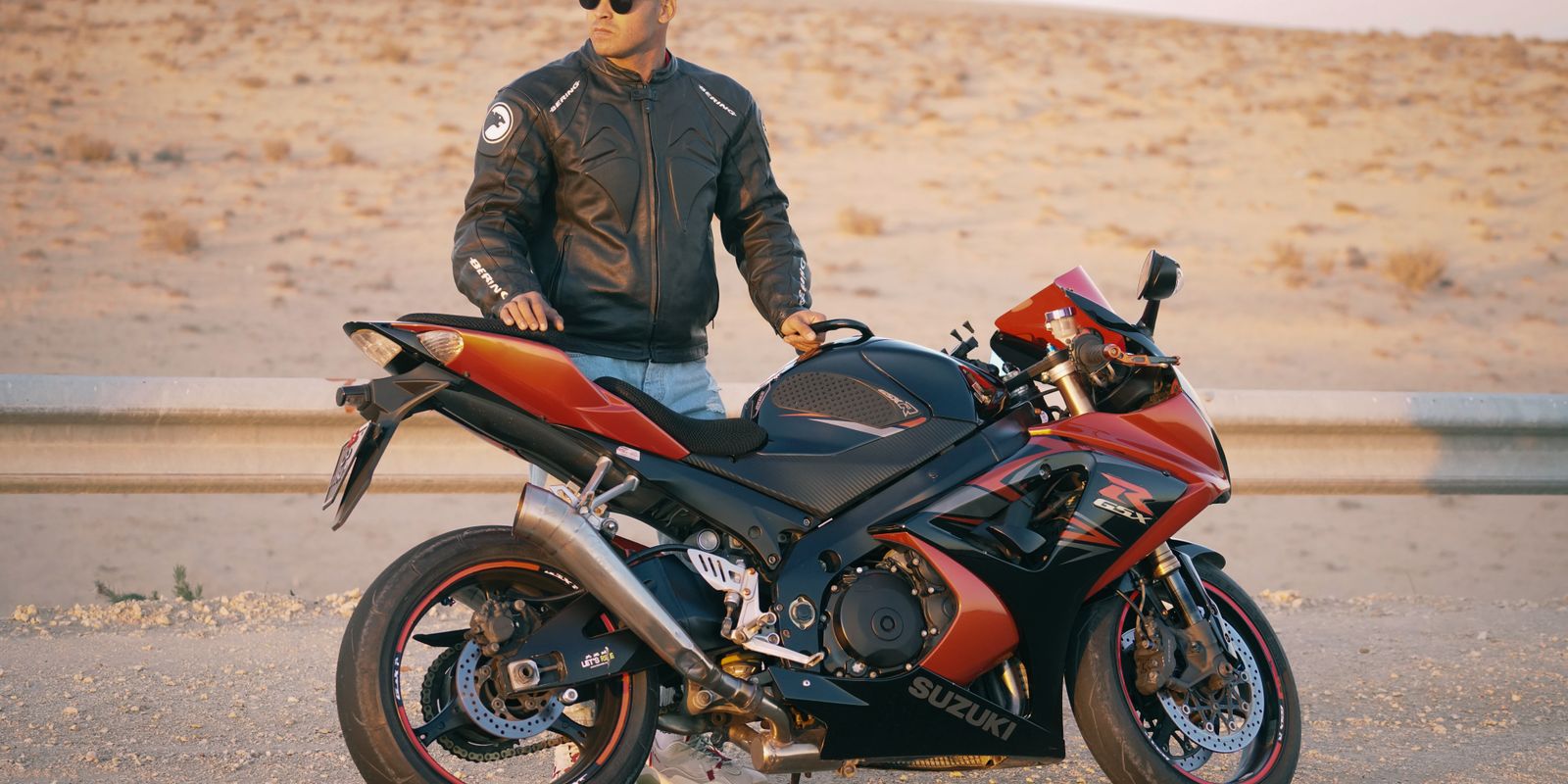 Férfi bőrdzsekiben és sapkában sportmotorral egy sivatagi úton