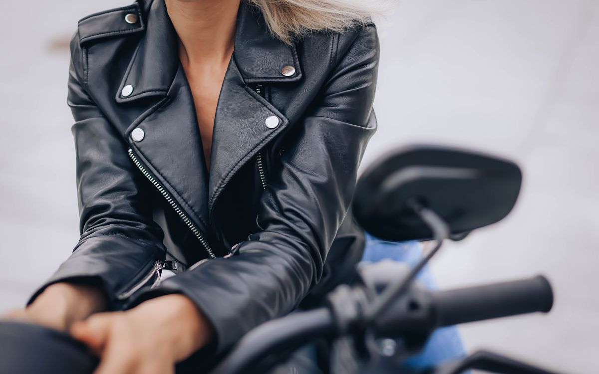 Közeli kép egy nőről fekete, állógalléros bőrkabátban motorozás közben