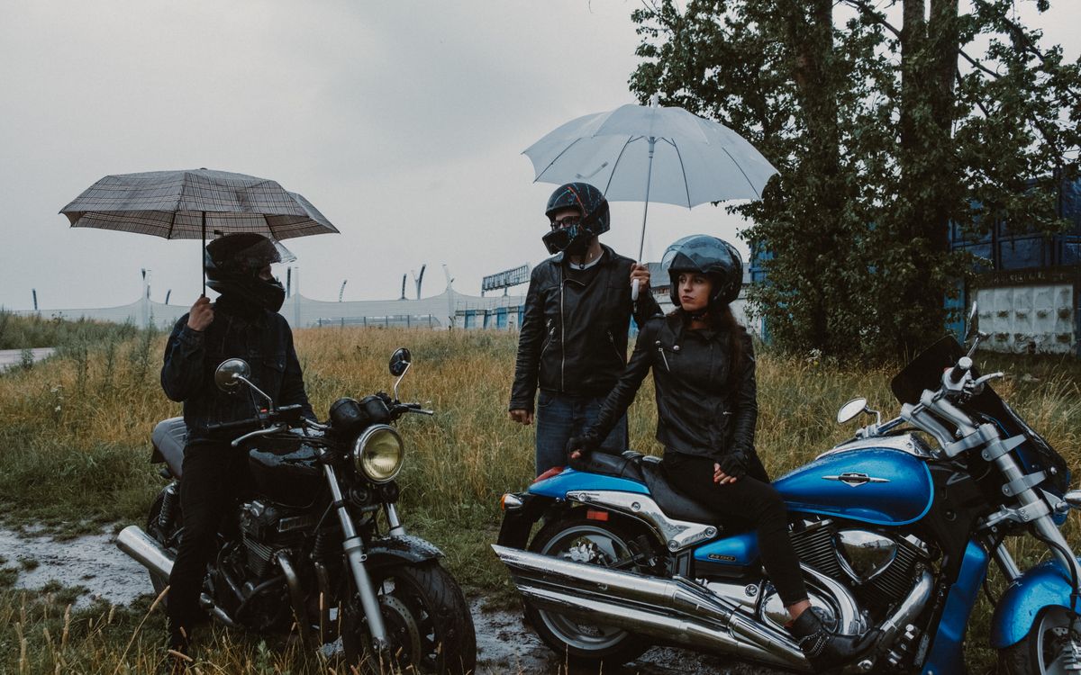 Motorosok esernyő alatt bújnak meg az eső elől egy füves mezőn