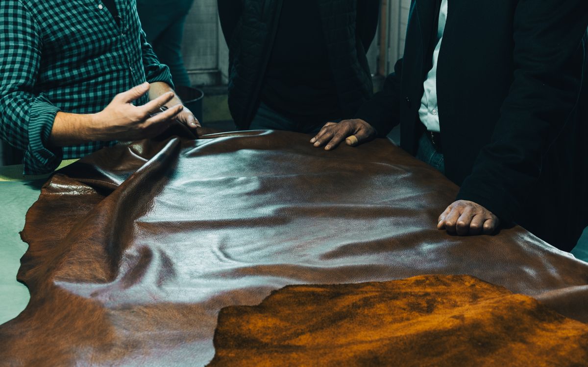 Bőrmegmunkálók egy csoportja bőrt vizsgál egy asztalon, a minőségre és az anyagválasztásra figyelve