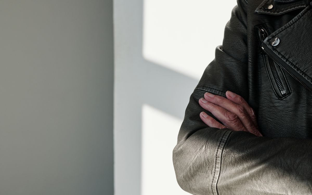 Közelkép keresztbe font karokról fekete bőrdzsekiben, súrló fényben