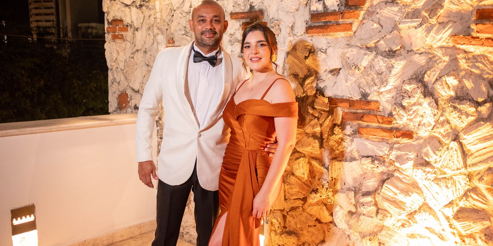 Elegáns pár estélyi öltözékben pózol egy megvilágított kőfal előtt