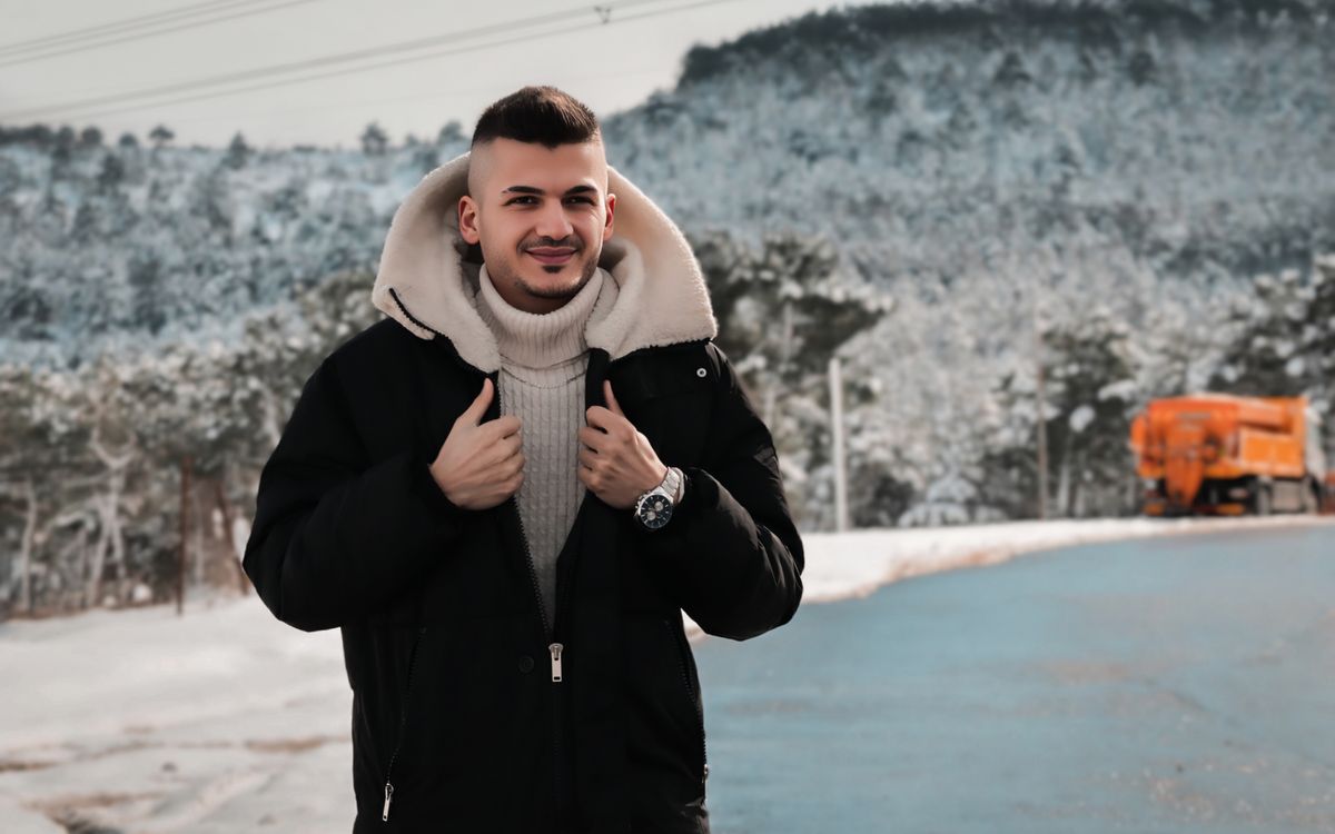 Fiatal férfi téli öltözékben egy havas erdő előtt