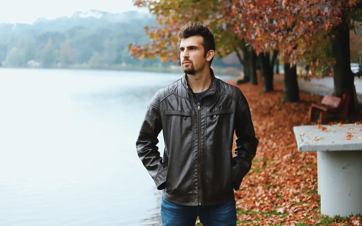 Egy szakállas férfi barna bőrkabátban egy tó partján ősszel