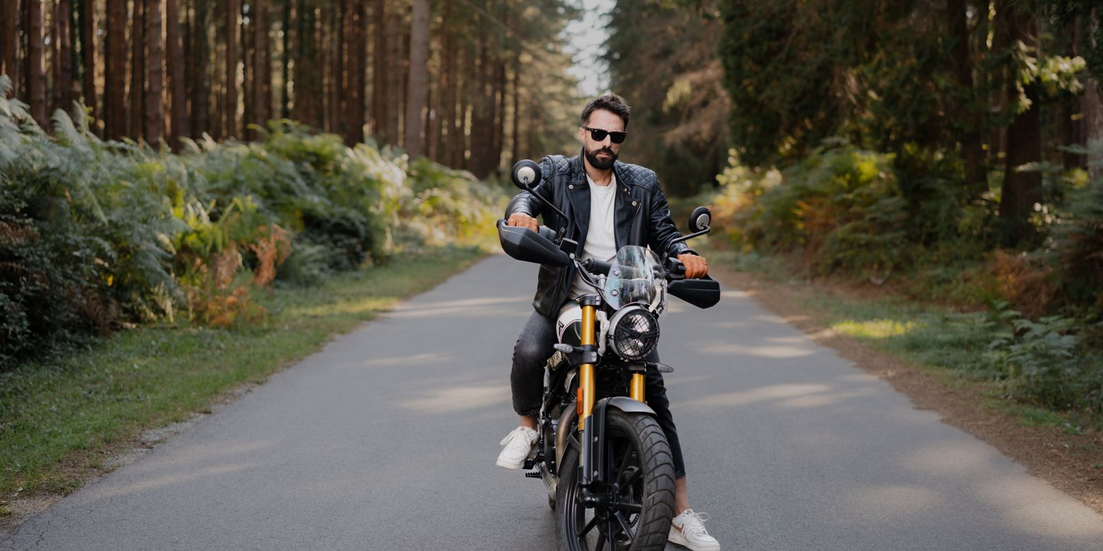 Motoros fekete bőrkabátban egy motoron egy erdei úton
